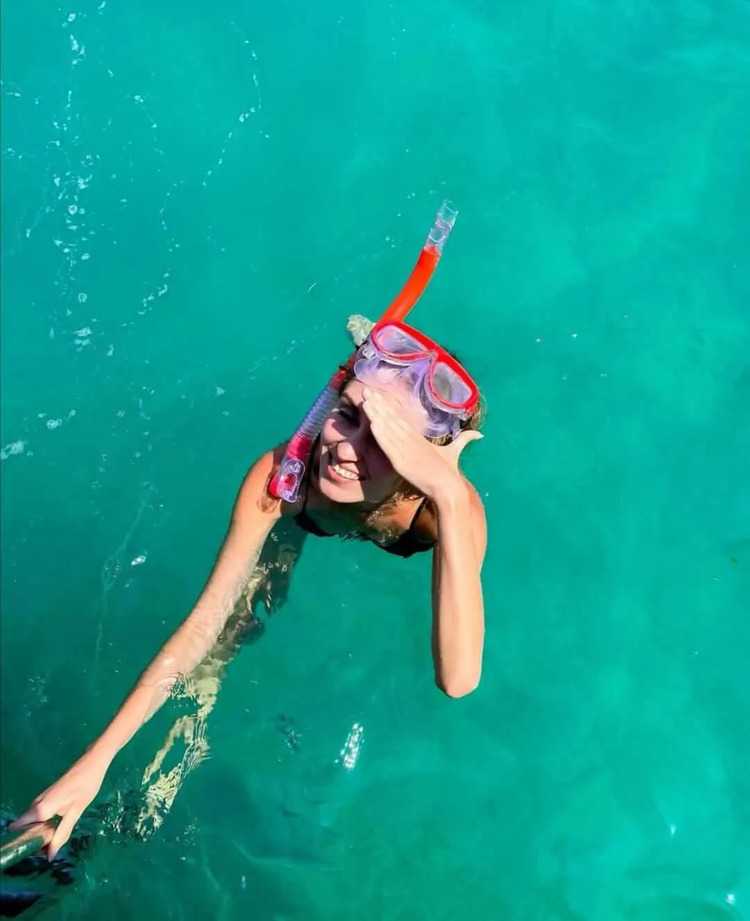 Mujer haciendo snorkel en el mar viendo a la cámara mientras cubre sus ojos de la luz del sol | Cancun Snorkeling