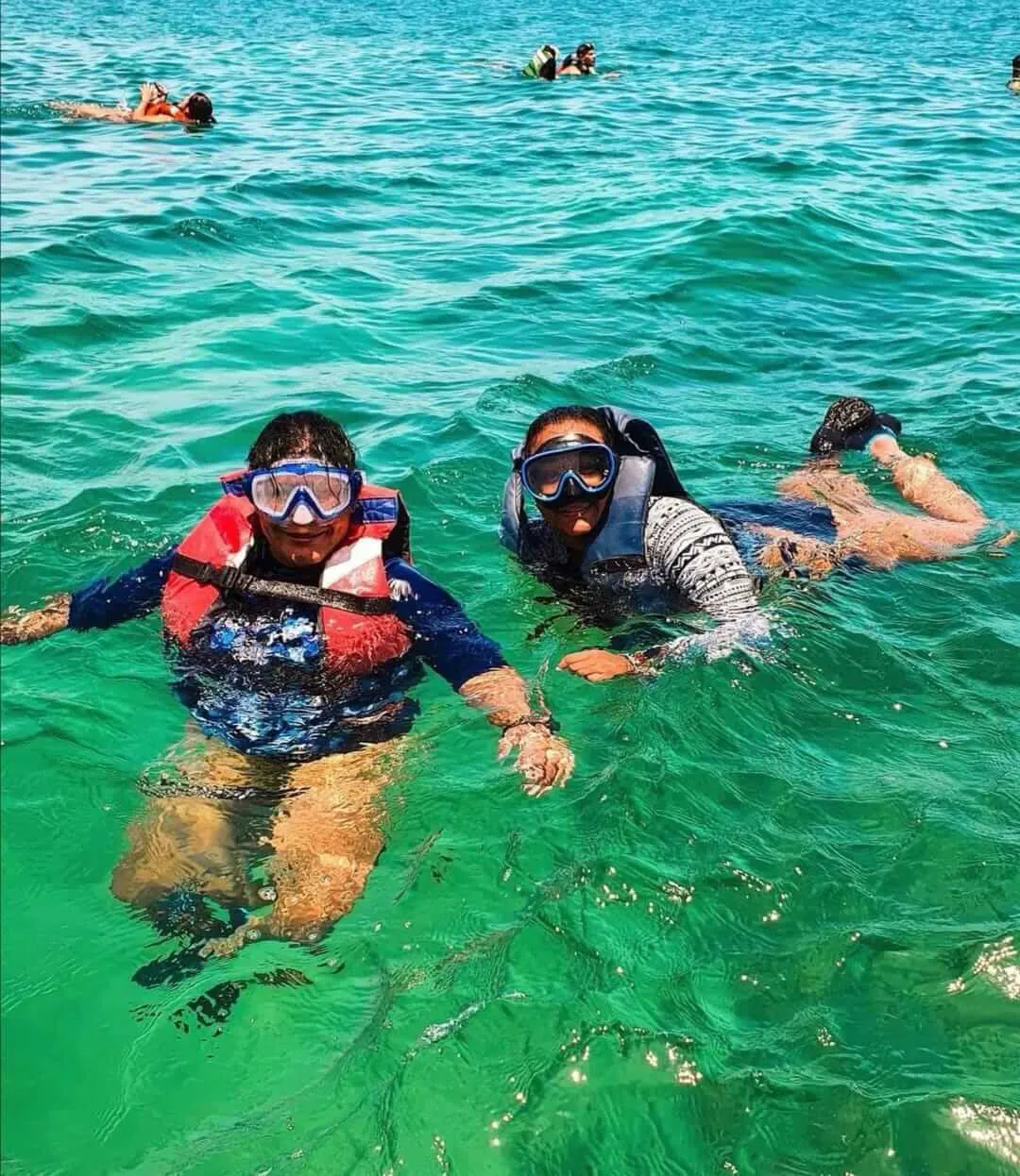 Dos mujeres haciendo snorkeling sonriendo a la camara mientras nadan con un grupo de personas | Cancun Snorkeling