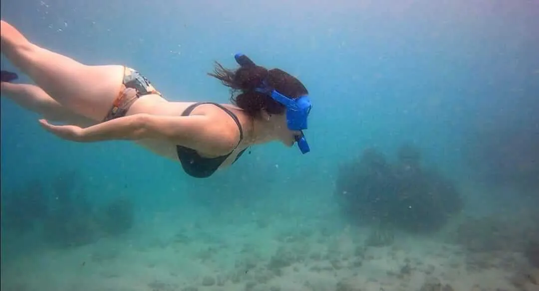 Vista lateral de una mujer sumergiendose en el mar usando una máscara de snorkel | Cancun Snorkeling
