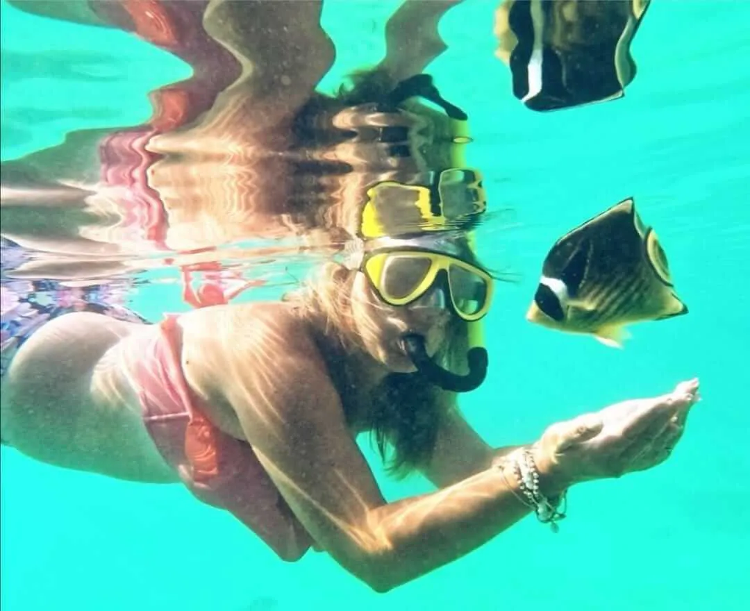 Mujer haciendo snorkel en la superficie posando a lado de un pez | Cancun Snorkeling