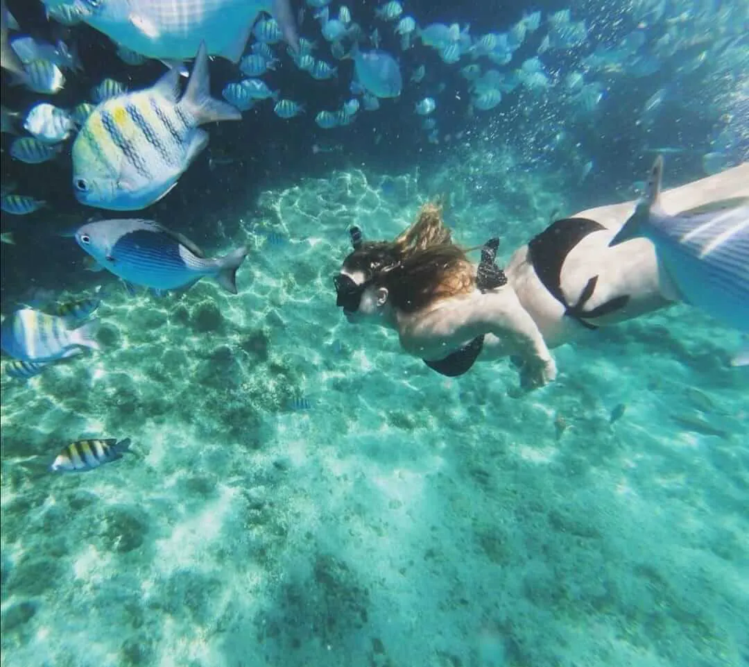Woman with black swimsuit snorkeling among a fish shoal