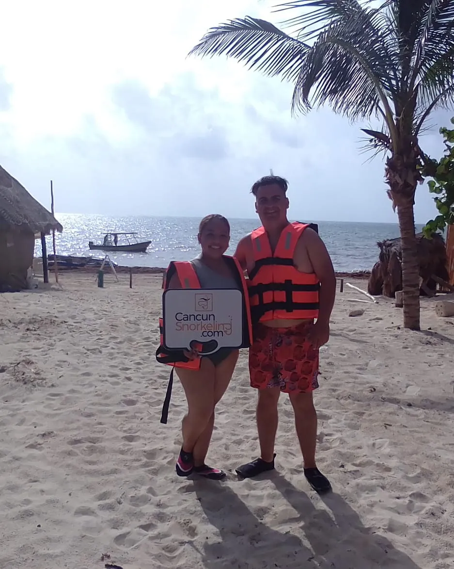 Una pareja parada en la playa con un bote y el mar de fondo | Cancun Snorkeling