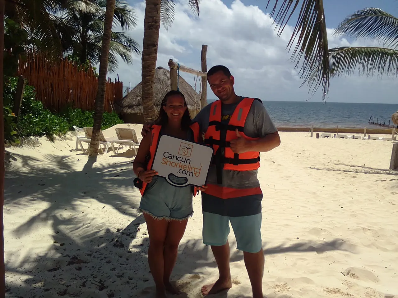 Pareja parada dezcalza en la playa bajo la sombre de una palmera | Cancun Snorkeling
