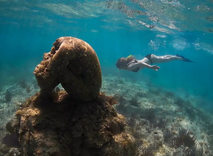 Woman swimming behind an underwater sculpture made artificial coral reef part of MUSA Underwater Museum